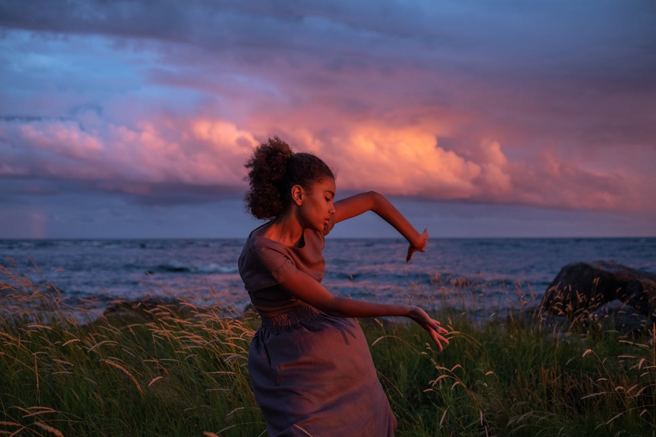 A woman gracefully dances by the sea at sunset, capturing emotion and natures beauty.