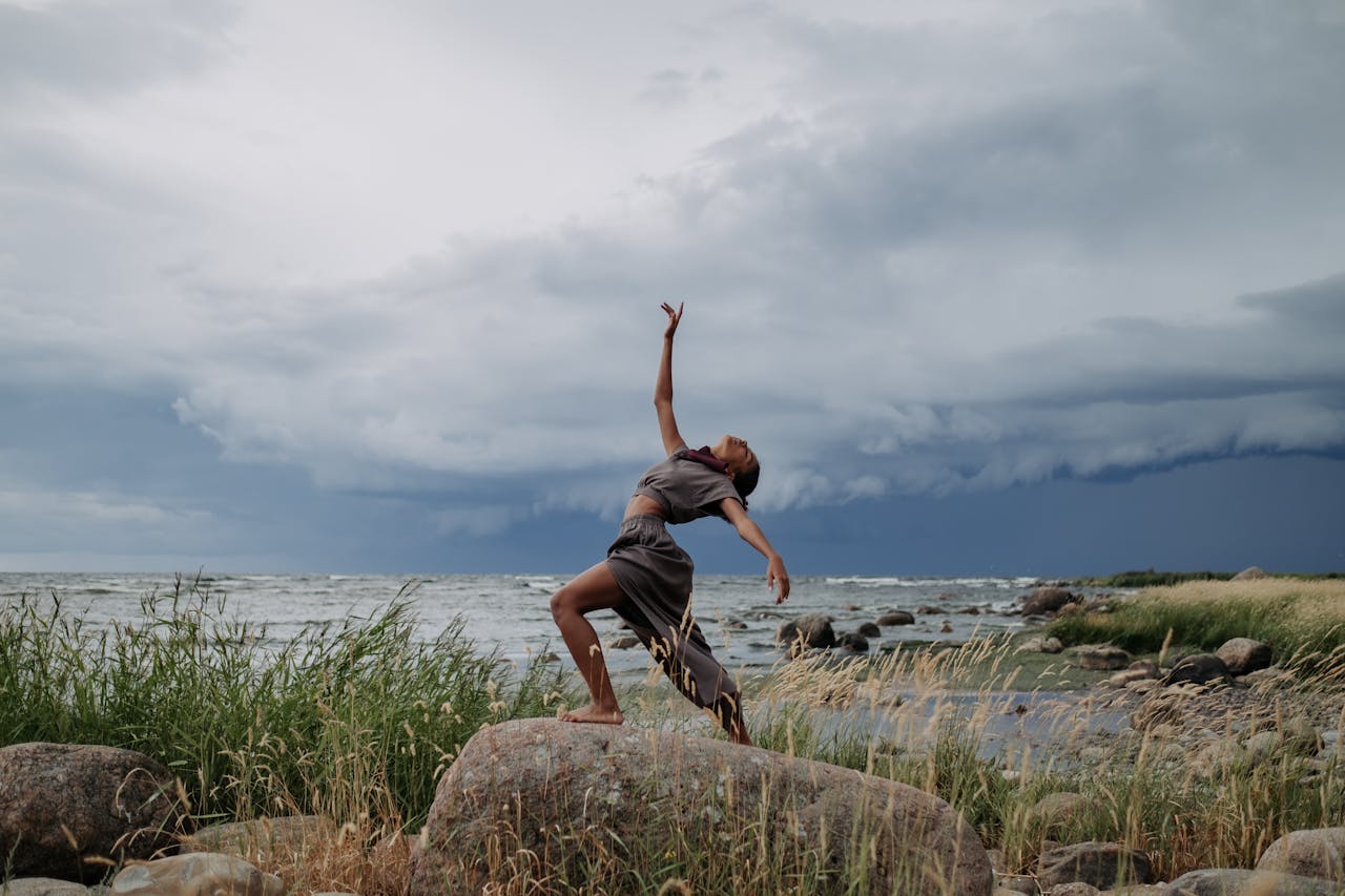 A woman performs a captivating dance on rocky seashore amidst dramatic storm clouds.