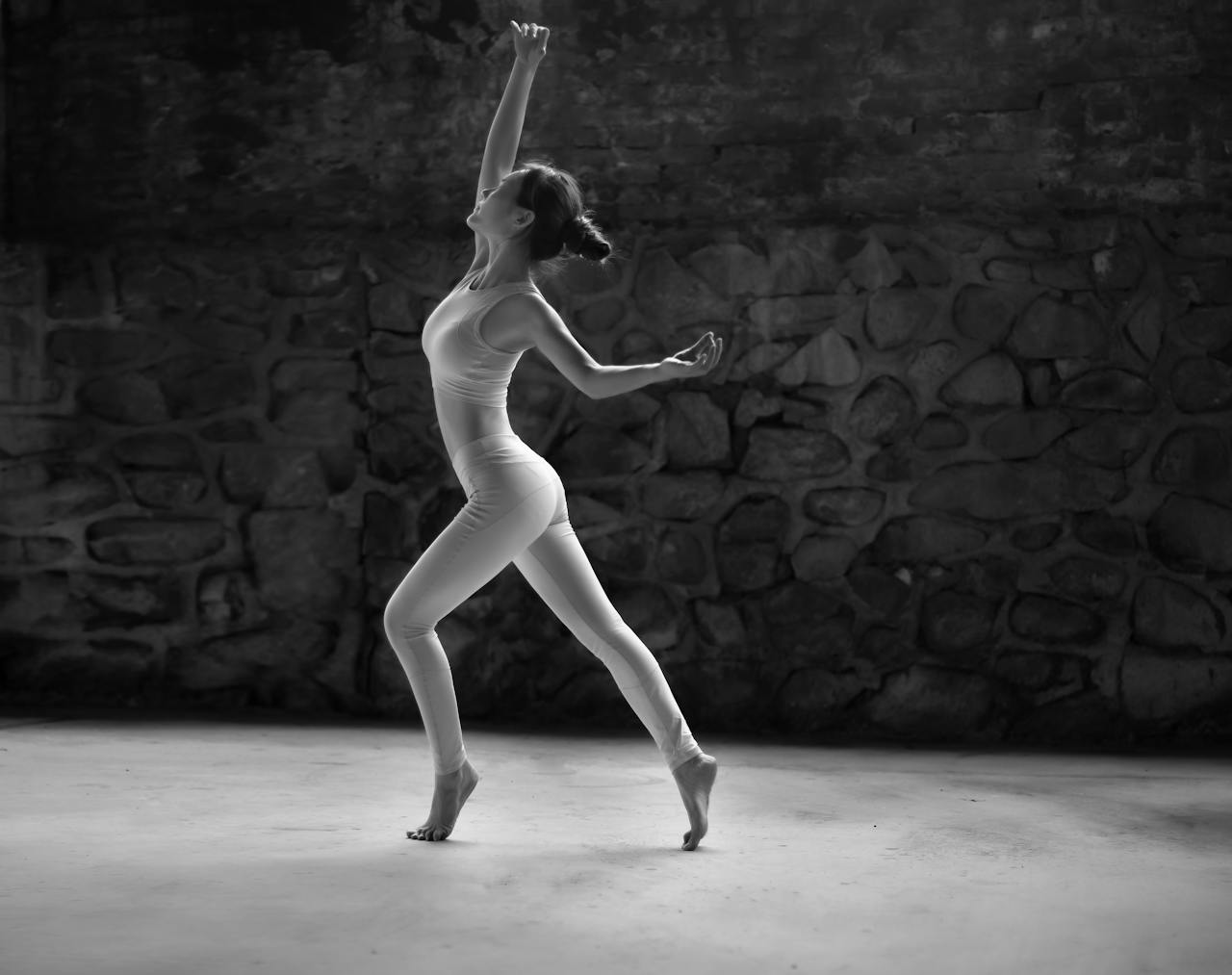 A woman in a dance pose wearing white, showcasing grace and movement in a studio setting.